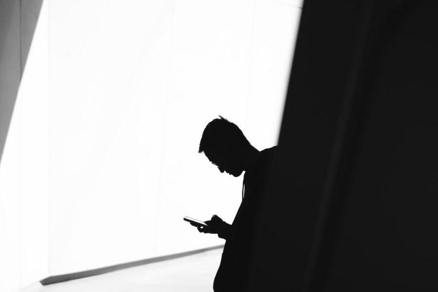 person using phone leaning on wall in silhouette photography