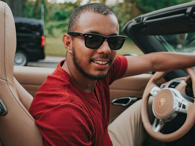 man in red crew neck shirt wearing black sunglasses sitting on driver seat