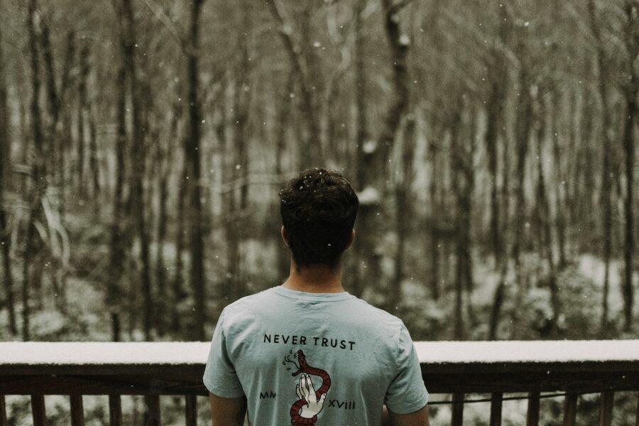 man wearing gray T-shirt standing beside brown wooden railing during snowy day
